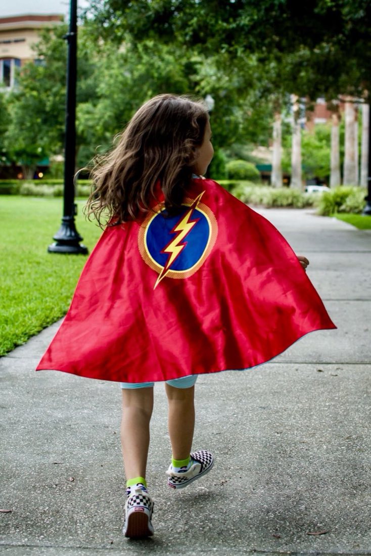 Young girl wearing a red superhero cape standing tall outdoors