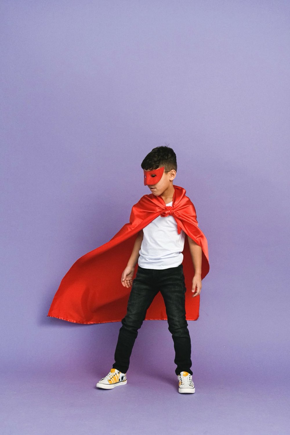 Smiling boy in a red superhero cape posing like a hero