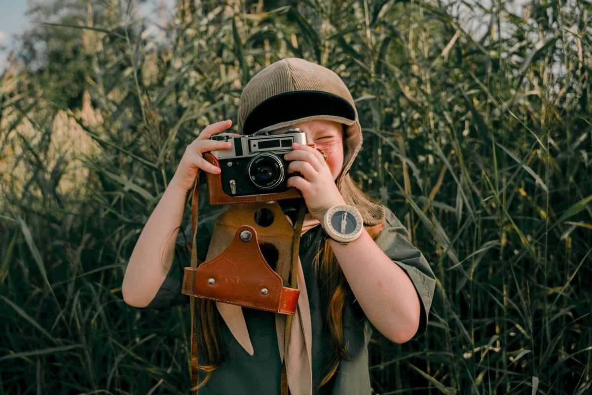 Child photographer holding a vintage camera in a meadow