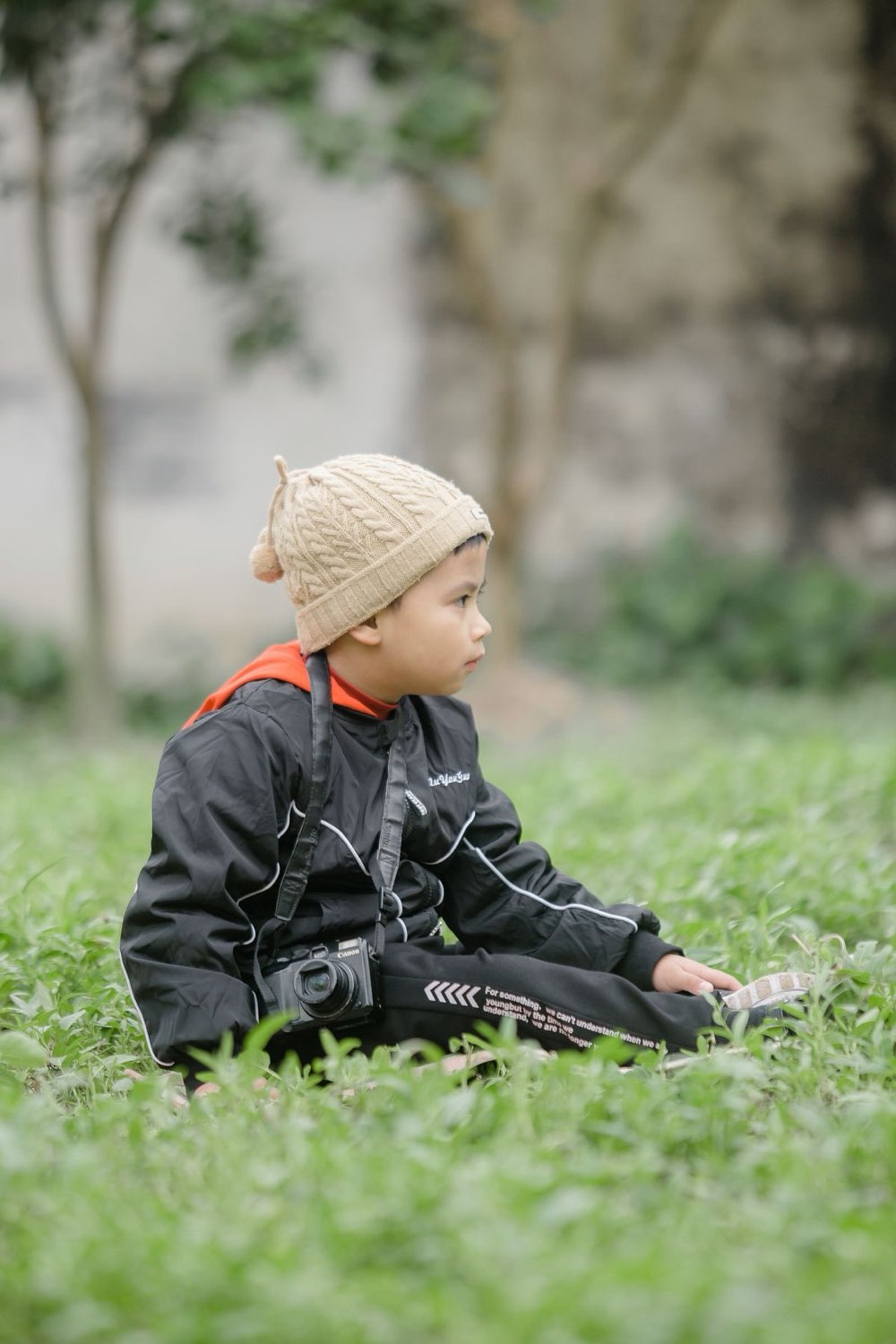 Toddler in a knit hat sitting in the grass at a city park