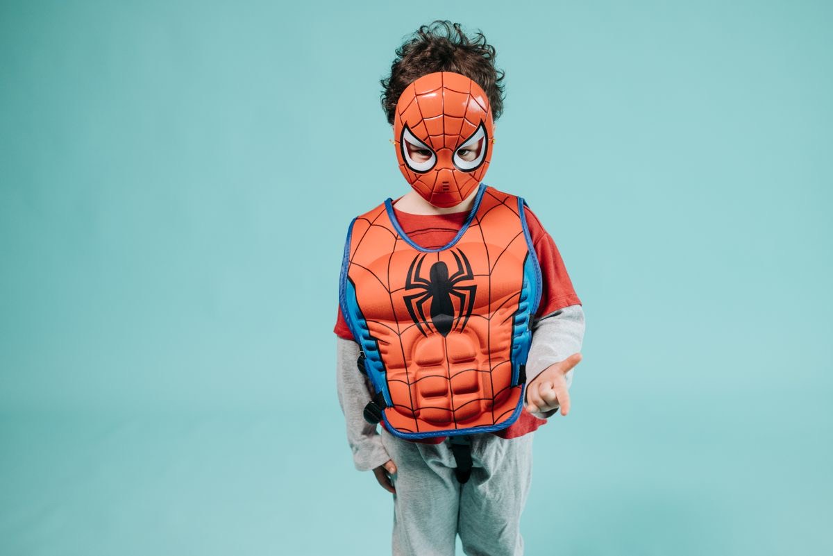 Boy in a superhero costume smiling against a bright studio background