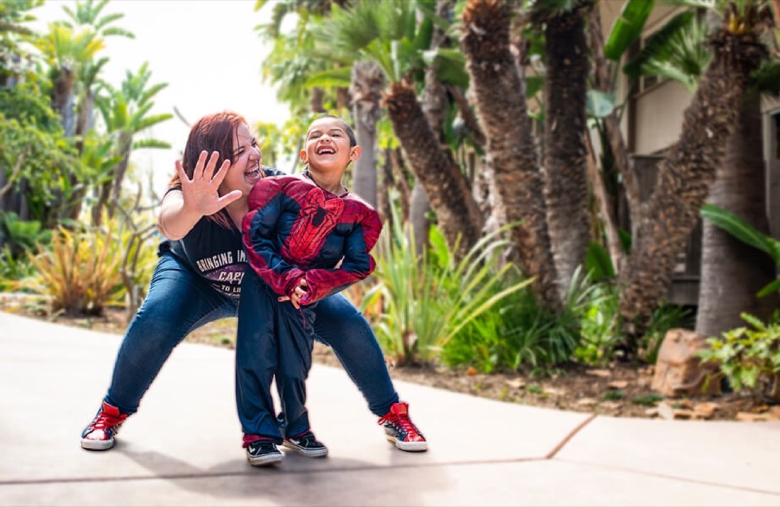 Child in a Spider-Man costume laughing with a Capes and Crowns volunteer during an Inspire Session